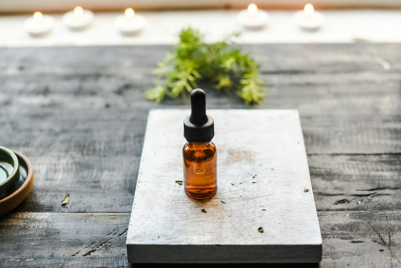 Amber glass dropper bottle on a wooden surface with greenery in the background.