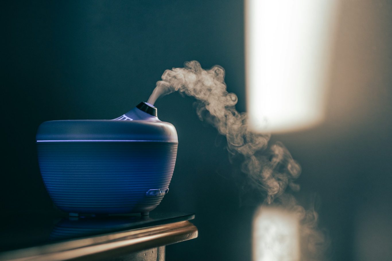 A blue diffuser releasing a gentle plume of aromatic mist in soft lighting.
