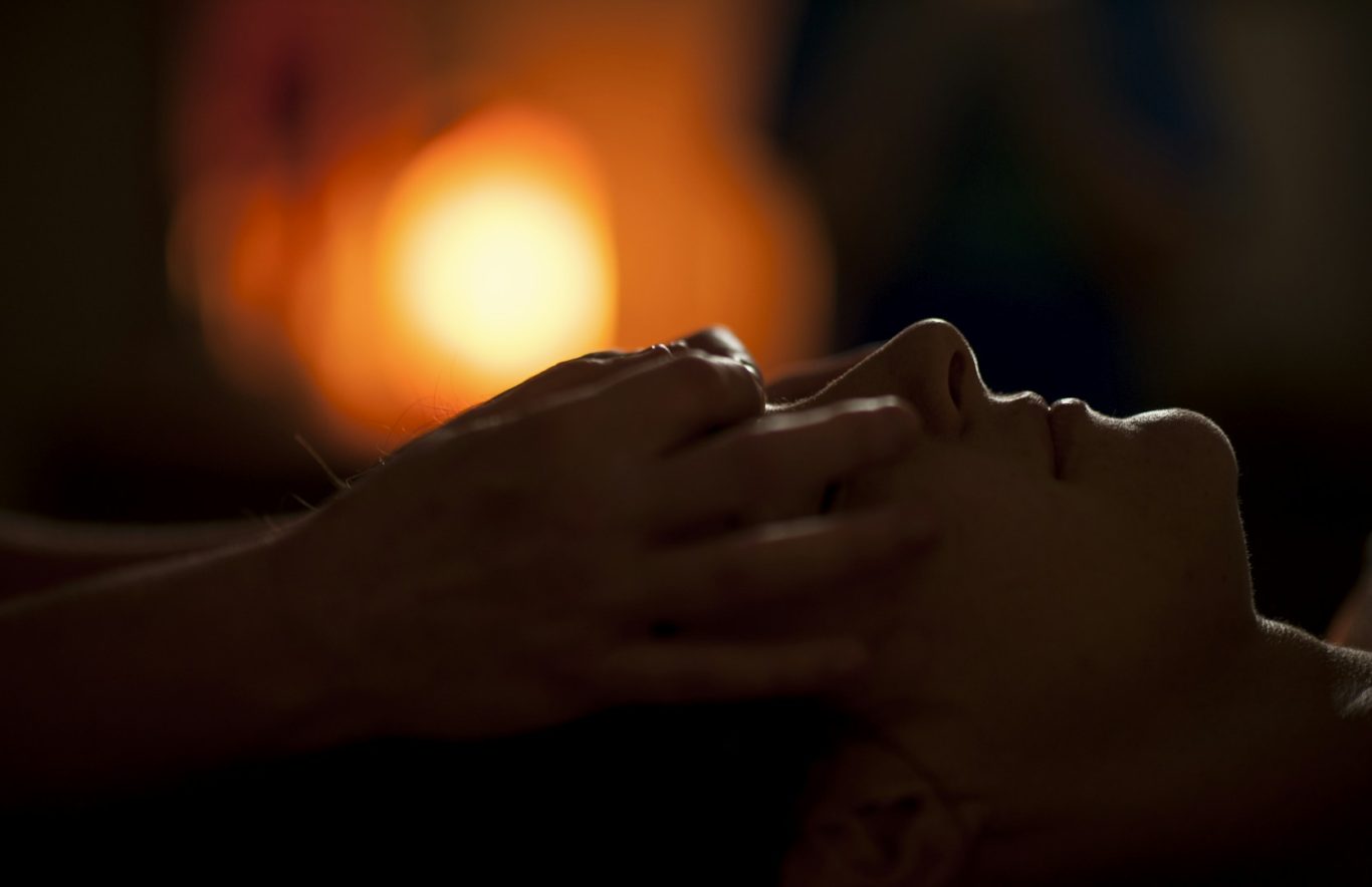 A person receiving a facial massage in warm, softly-lit surroundings.